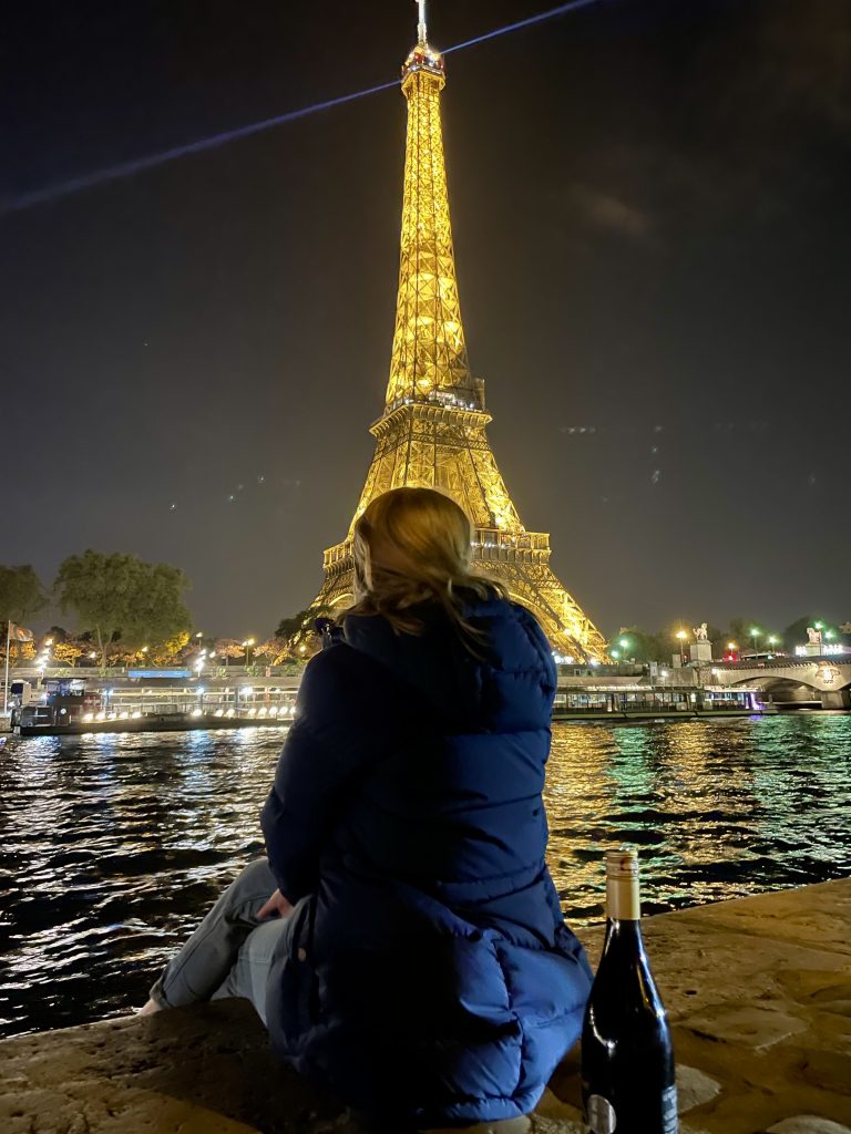 A woman sitting in front of the Eiffel Tower at night in the winter